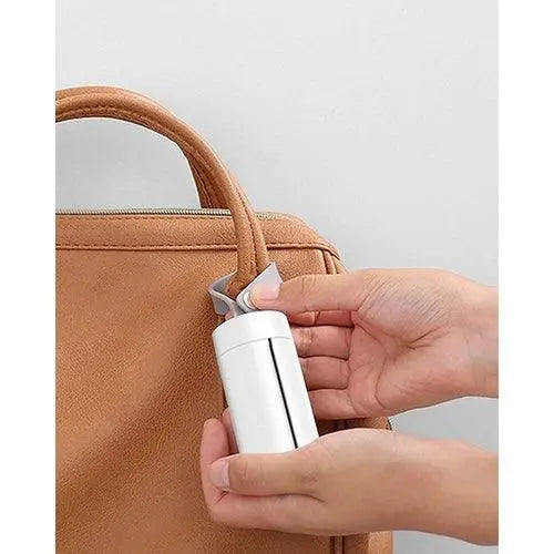 Hand attaching white portable pet waste bag dispenser to brown leather bag handle
